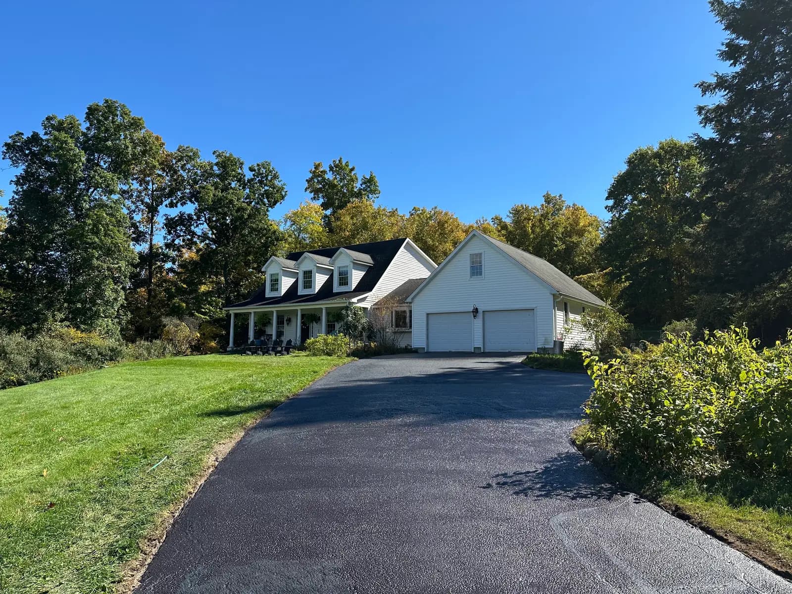 Freshly sealcoated asphalt driveway leading to a white home with a two-car garage