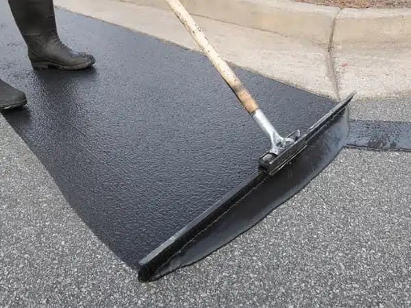 Sealer being squeegee-applied across asphalt pavement